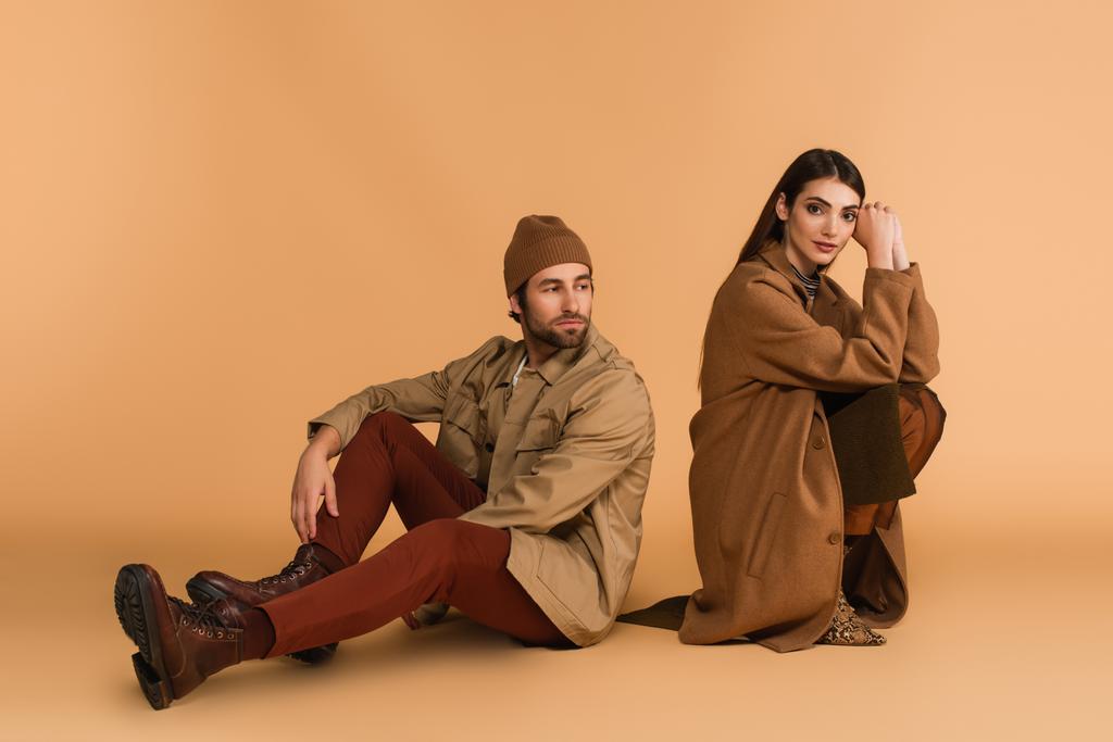 man in trendy autumn outfit sitting near fashionable woman on beige background - Foto, Imagem