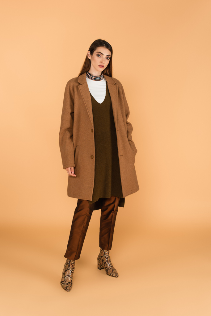 fashionable woman holding hand in pocket of trendy coat on beige background - Foto, imagen