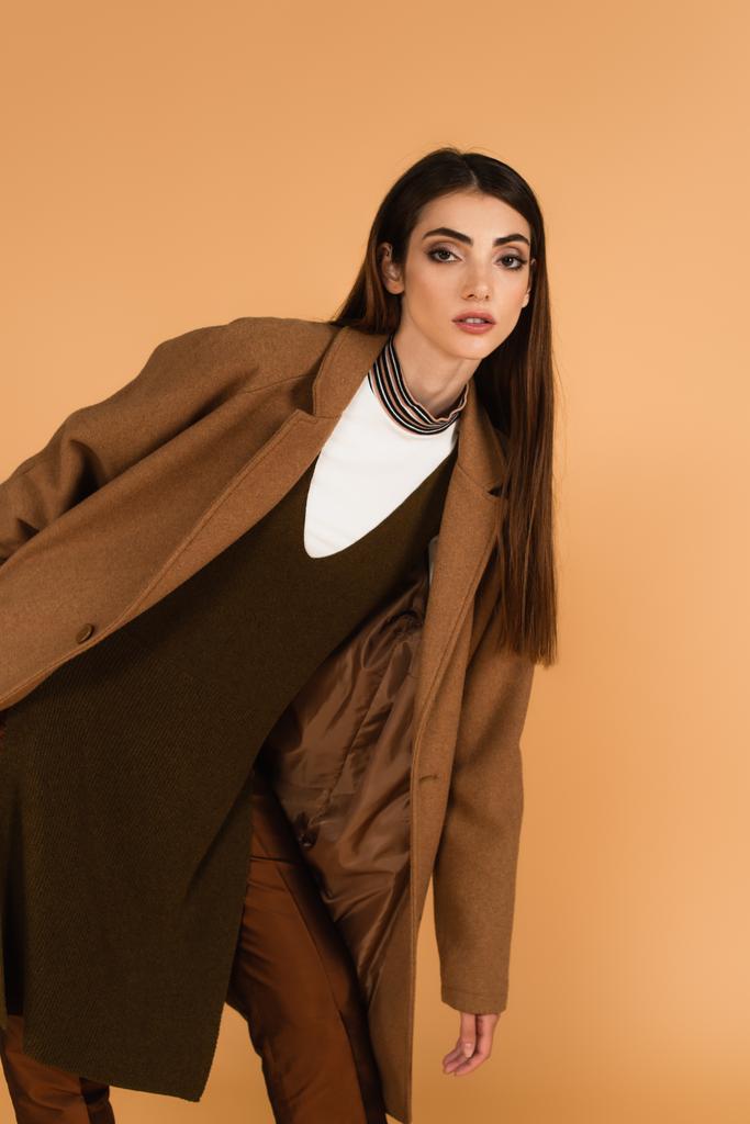 young brunette woman in brown coat looking at camera while posing isolated on beige - Photo, Image