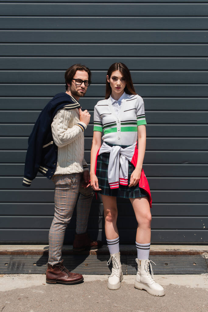 young couple in trendy clothes looking at camera near grey wall - Photo, image