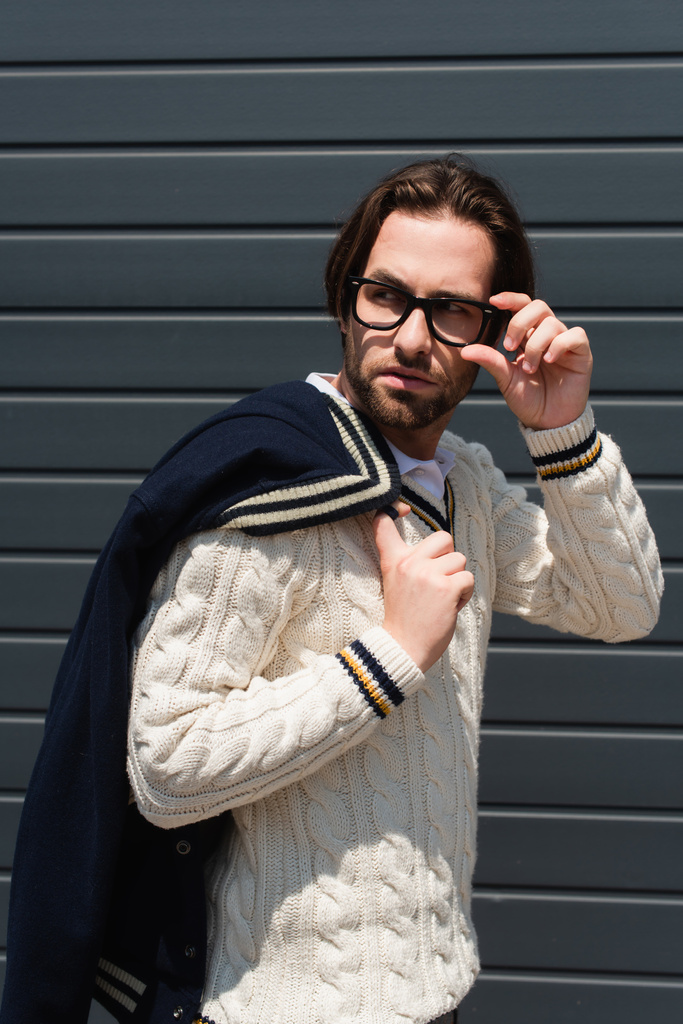 stylish man in white knitted pullover adjusting eyeglasses while looking away outdoors - Foto, Imagen