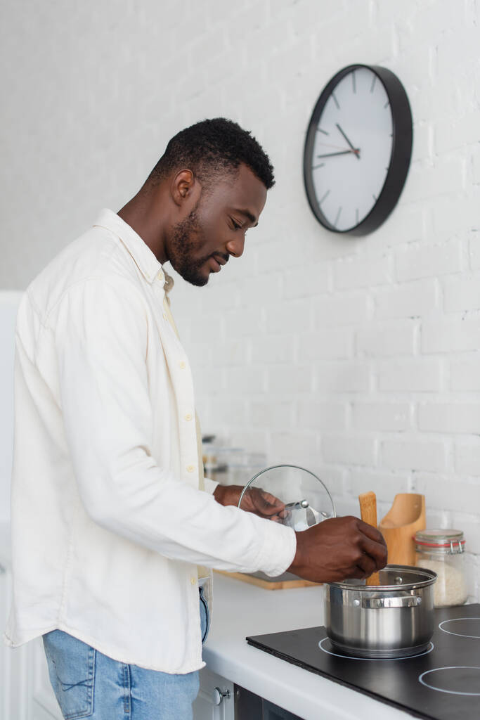 πλαϊνή όψη του νεαρού Αφροαμερικανού άνδρα που μαγειρεύει στην κουζίνα  - Φωτογραφία, εικόνα