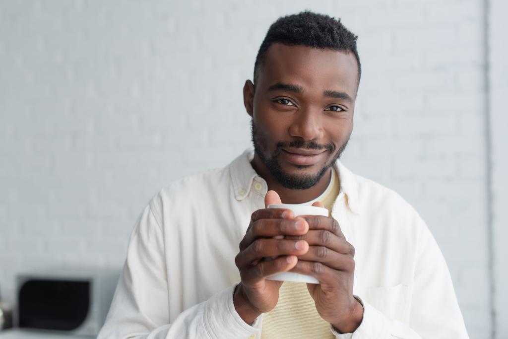wesoły Afroamerykanin mężczyzna trzyma filiżankę kawy rano  - Zdjęcie, obraz