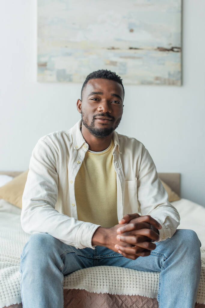 young african american man with clenched hands sitting on bed - Photo, Image