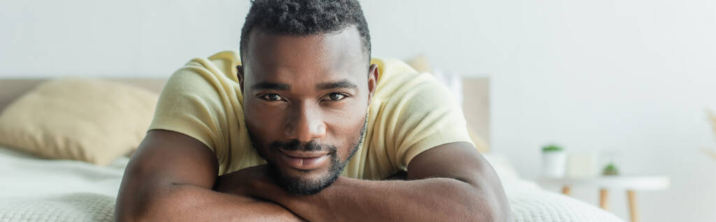 szakállas afro-amerikai férfi pólóban feküdt az ágyon, banner - Fotó, kép