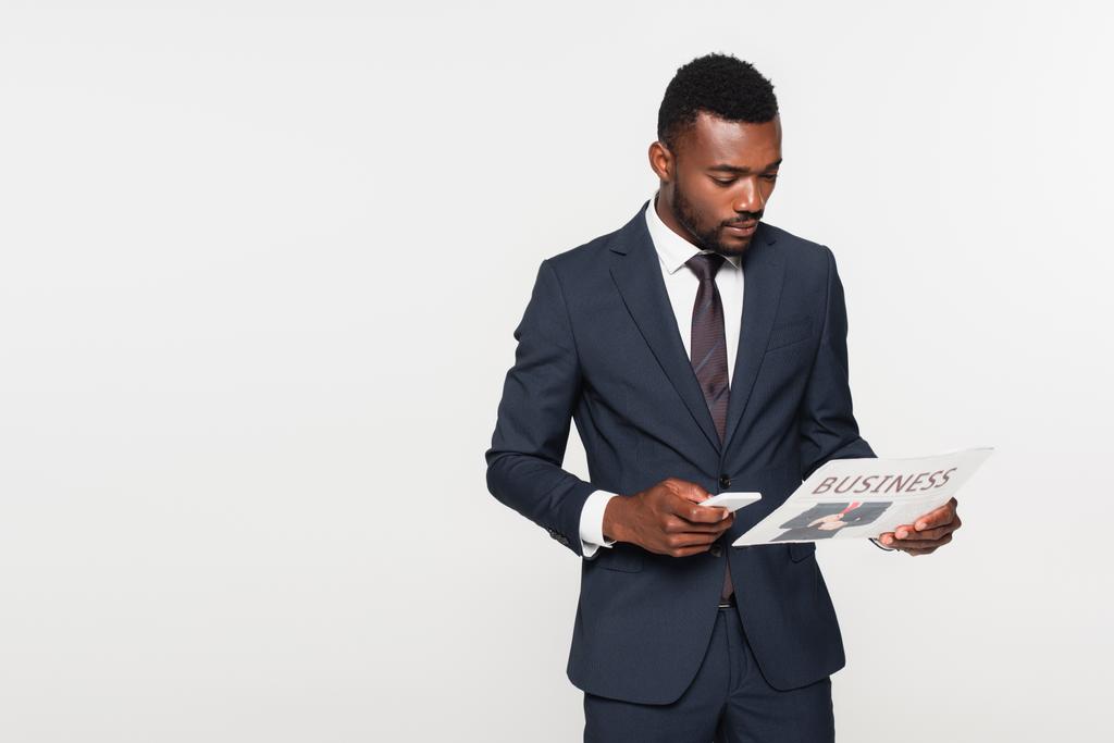 uomo d'affari afroamericano in giacca e cravatta con smartphone mentre leggeva il giornale isolato su grigio - Foto, immagini