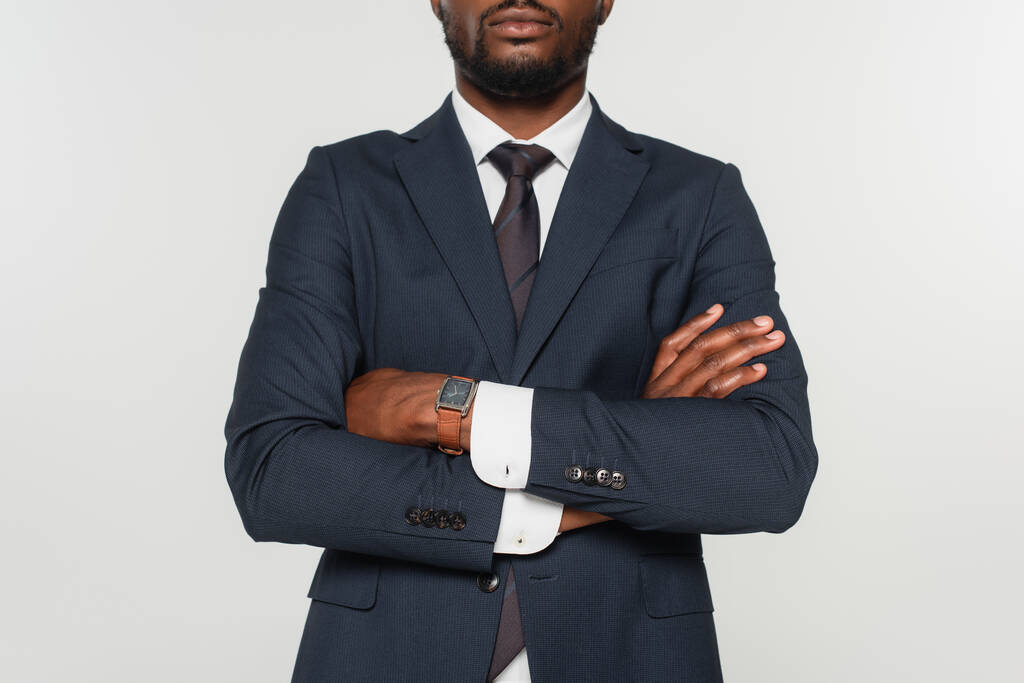 vista ritagliata dell'uomo afroamericano in giacca e cravatta in piedi con braccia incrociate isolate su grigio - Foto, immagini