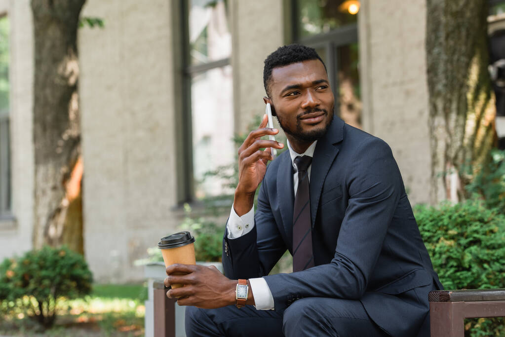 bearded african american businessman talking on mobile phone and holding coffee to go outside  - Photo, Image
