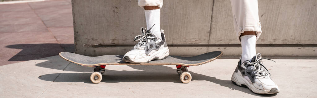 частичный вид человека в кроссовках возле скейтборда на городской улице, баннер - Фото, изображение