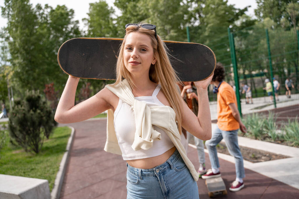 красива блондинка зі скейтбордом дивиться на камеру на відкритому повітрі
 - Фото, зображення