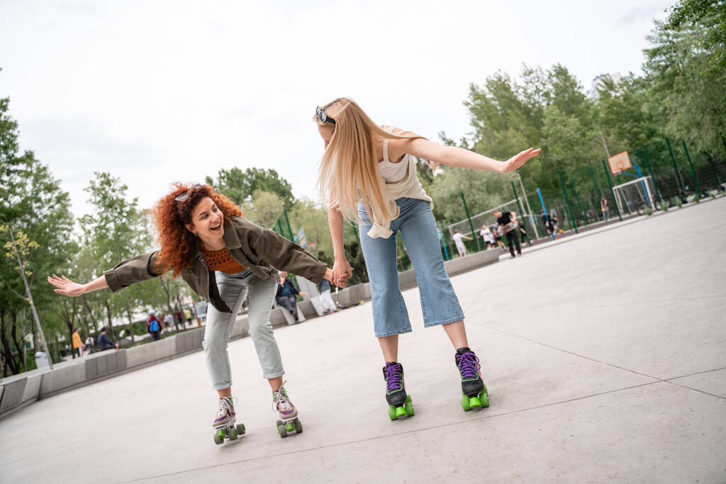 happy friends holding hands while rollerblading in skate park - Photo, Image