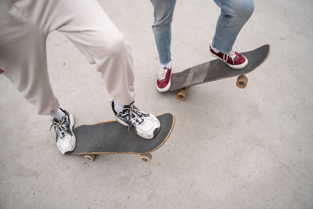 abgeschnittene Ansicht von Freunden in Turnschuhen, die im Freien Skateboards fahren - Foto, Bild