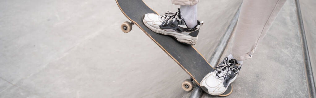 vista parziale dell'uomo in scarpe sportive equitazione skateboard sulla rampa di skate, banner - Foto, immagini