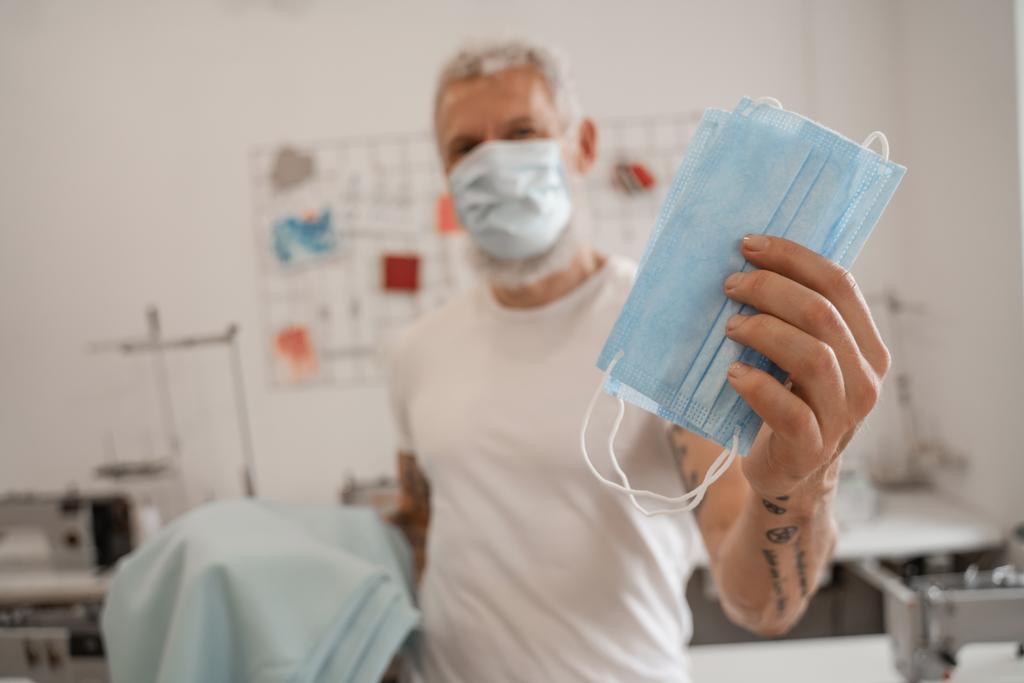 Alfaiate desfocado segurando máscaras médicas no atelier  - Foto, Imagem