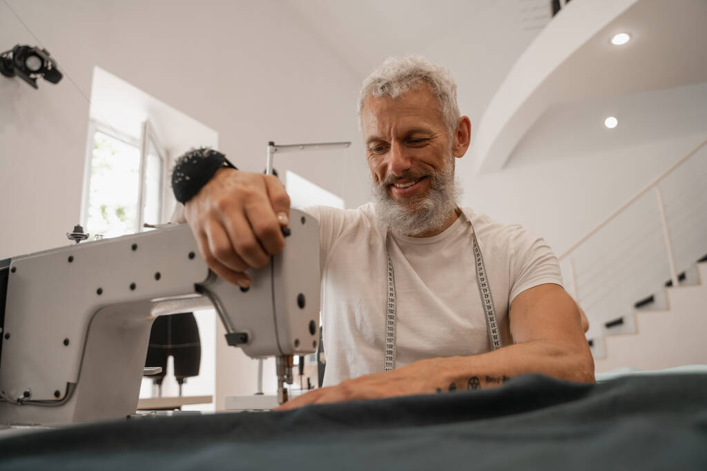 Smiling tailor sewing blurred cloth in designer studio  - Photo, Image