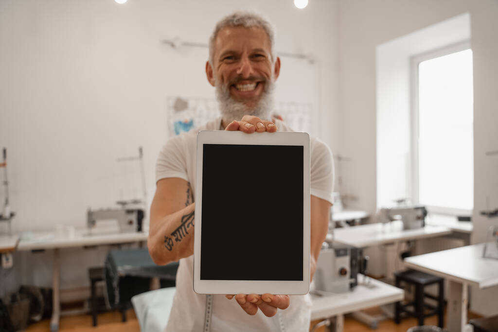Sonriente diseñador borroso sosteniendo tableta digital con pantalla en blanco  - Foto, Imagen