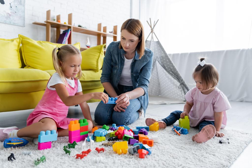 kindergarten teacher playing building blocks with preschooler girl and toddler kid with down syndrome  - Photo, Image