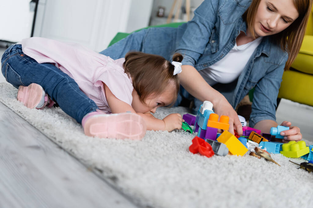 enfant en bas âge avec le syndrome du duvet jouer avec le professeur de maternelle sur le tapis  - Photo, image