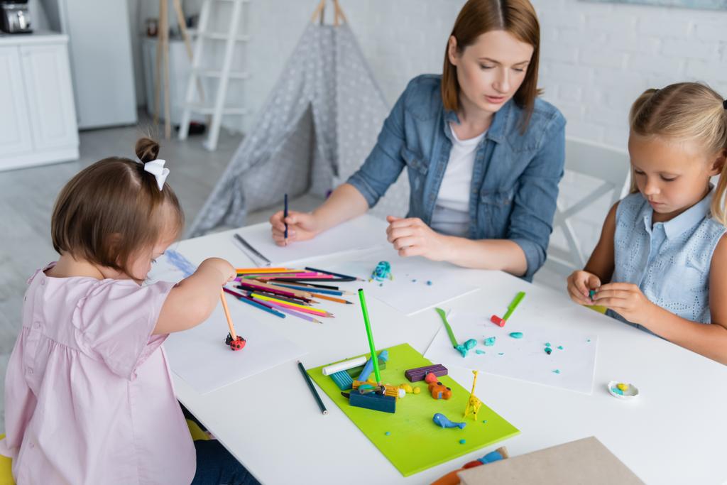 enfant handicapé tenant crayon avec plasticine près de l'enseignant et la fille à la maternelle  - Photo, image