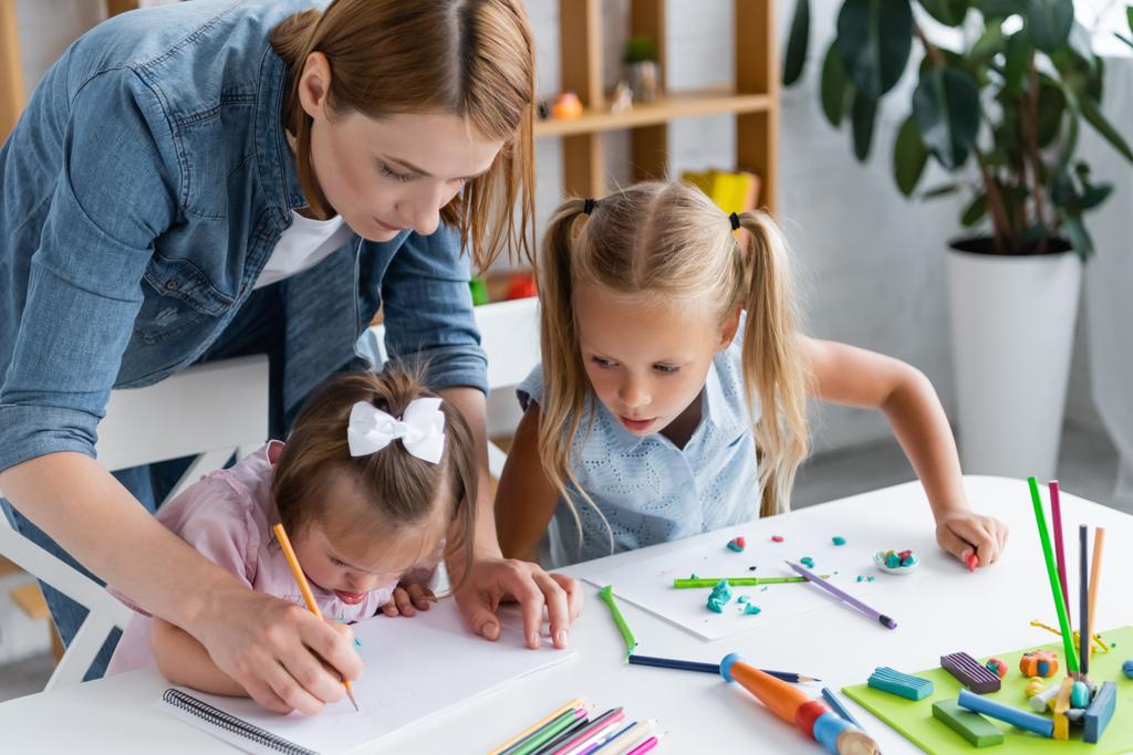 вчителька, яка допомагає дитині з синдромом Дауна малювати в приватному дитячому садку
  - Фото, зображення