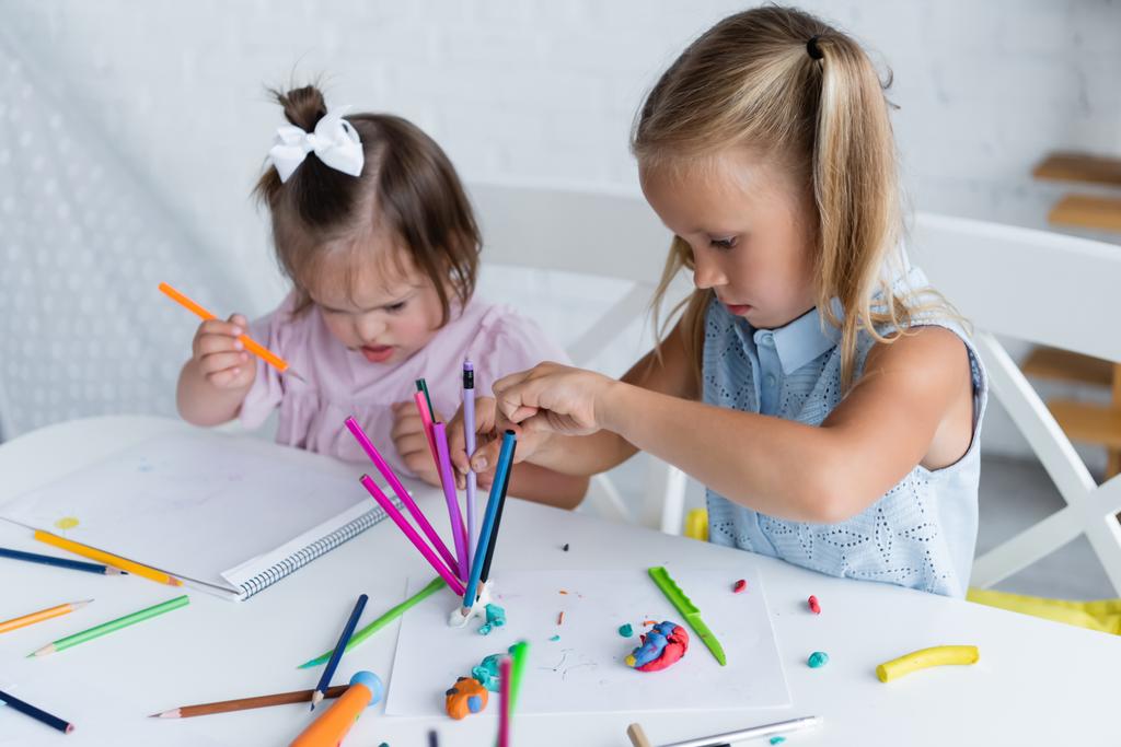 blondýny dívka dosažení barvy tužky v blízkosti zdravotně postižené batole dítě s dolů syndromem v soukromé mateřské školce  - Fotografie, Obrázek