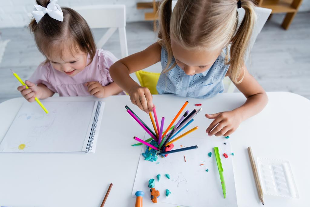високий кут зору дівчинки дошкільника і малюка з синдромом Дауна малюючи в дитячому садку
  - Фото, зображення