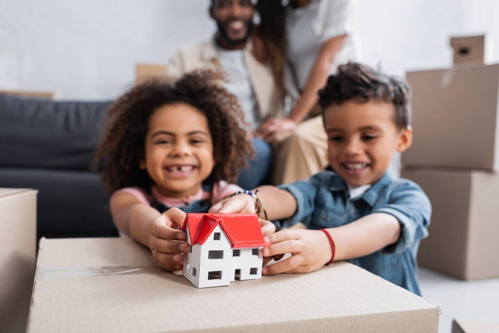 cheerful african american kids near house model and parents on blurred background - Photo, Image