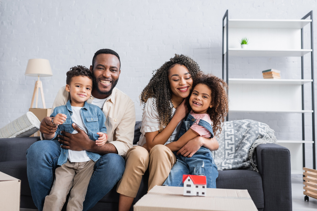 Afrykańska amerykańska rodzina siedzi na kanapie w pobliżu domu model na pudełku kartonowym - Zdjęcie, obraz