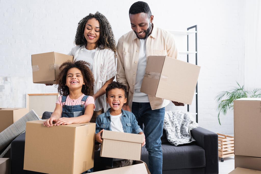 eccitata famiglia afroamericana in possesso di pacchetti di cartone in un nuovo appartamento - Foto, immagini