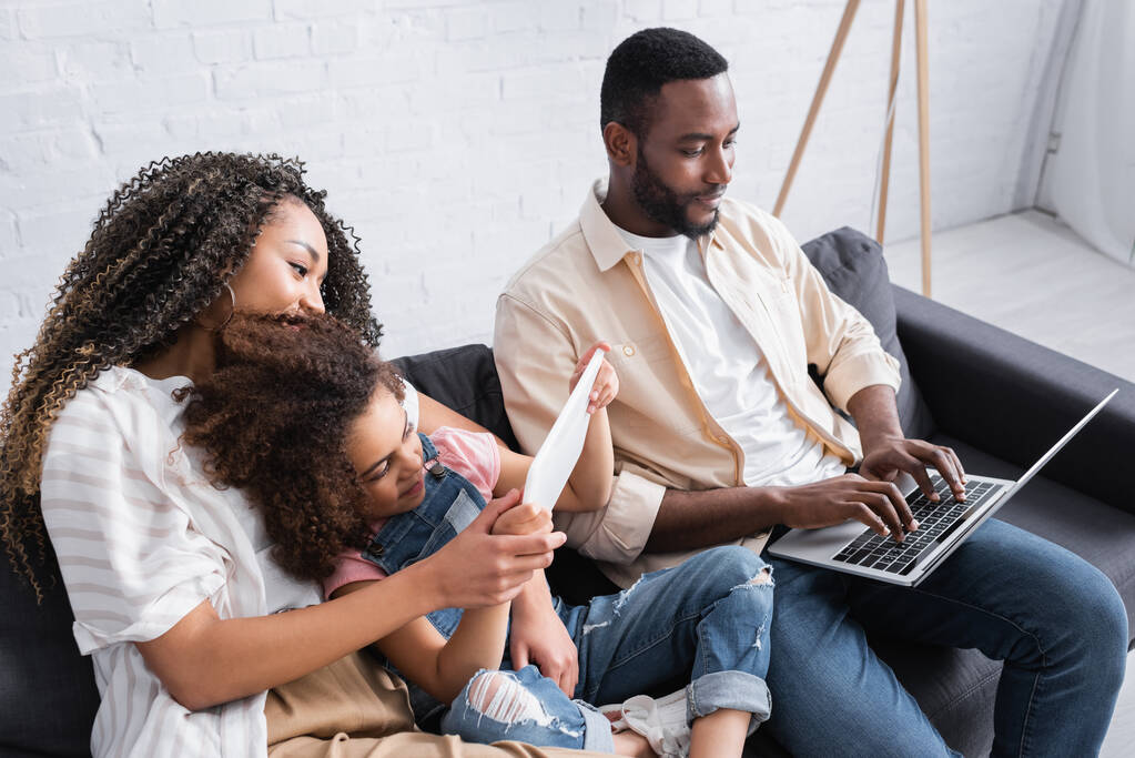 Afroamerykanka dziewczyna za pomocą laptopa w pobliżu matki i taty wpisując na laptopie - Zdjęcie, obraz