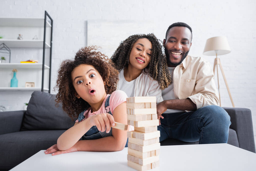 amazed african american kid playing wood blocks game near smiling parents - Photo, Image
