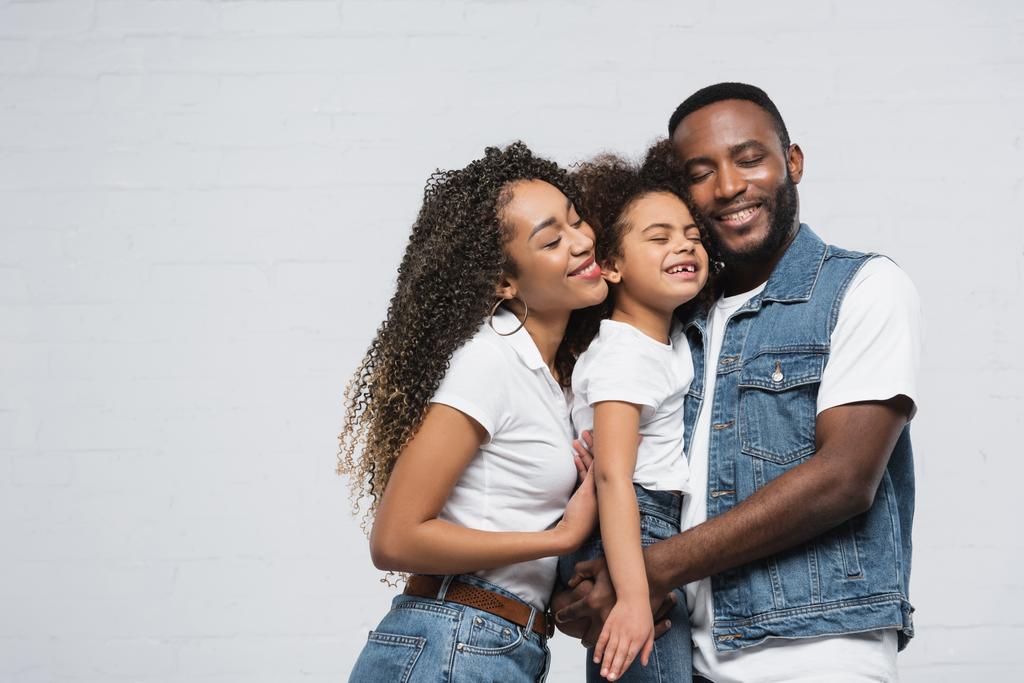 glückliche afrikanisch-amerikanische Familie umarmt mit geschlossenen Augen auf grau - Foto, Bild