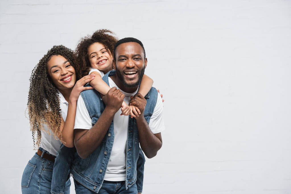 happy african american family looking at camera while hugging on grey - Photo, Image