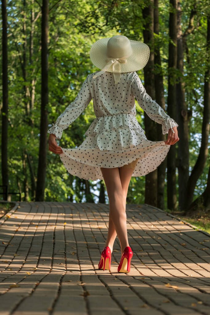 woman in short summer dress, wide hat, stockings and high-heeled shoes in the morning in the park - Fotoğraf, Görsel