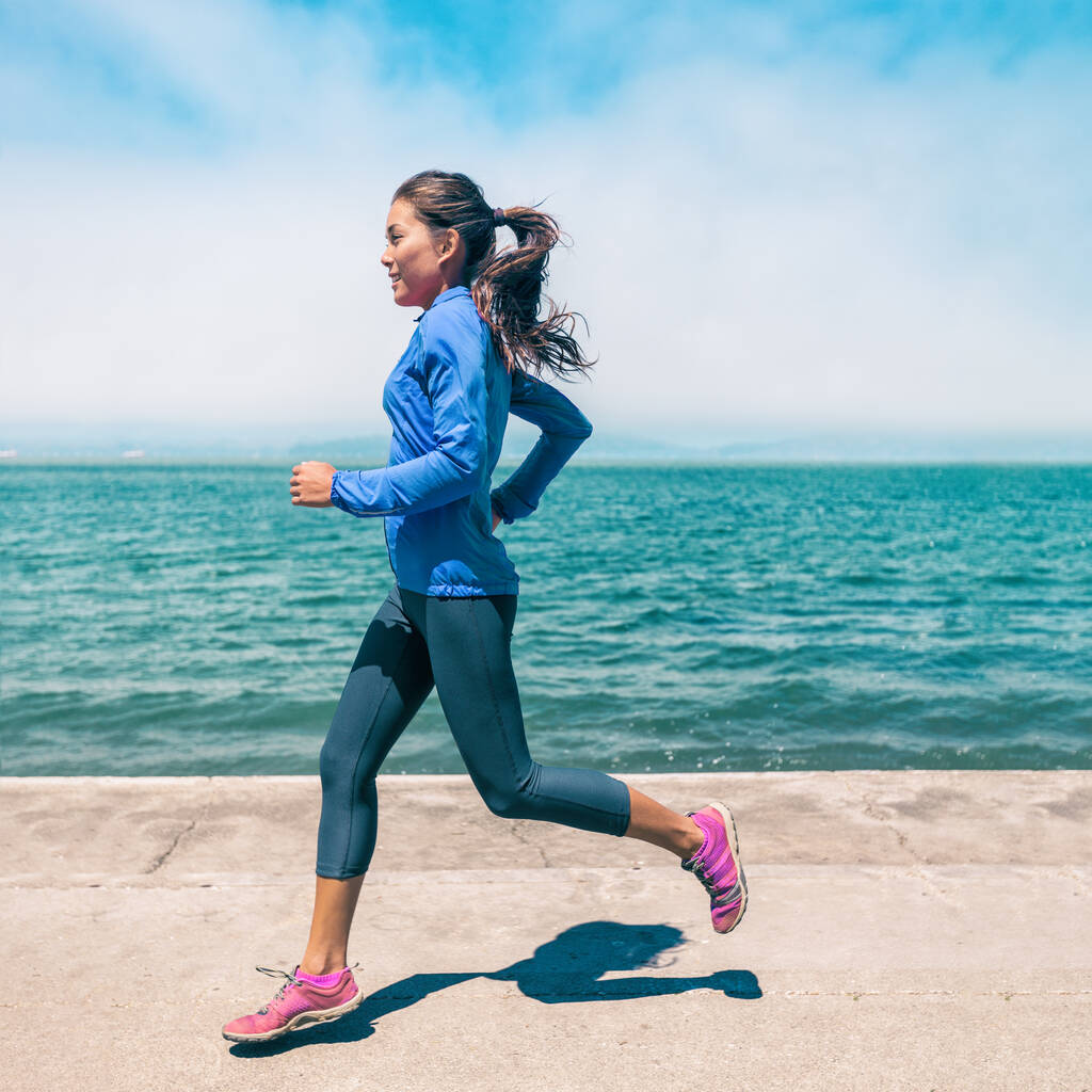 atleta de corrida mulher asiática correndo pela praia vestindo azul blusão perneiras e sapatos. Treinamento ao ar livre na primavera pelo mar. Retrato de perfil de culturas quadradas. - Foto, Imagem