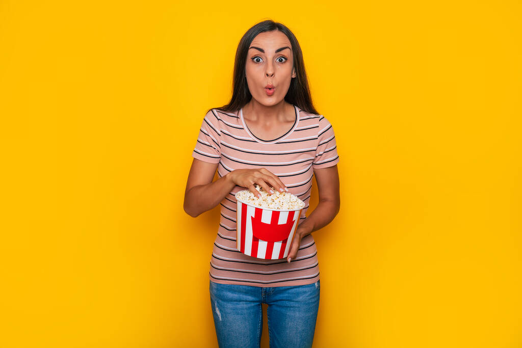 Podekscytowany piękna młoda brunetka kobieta w luźnym stroju i okulary kina 3D i duży kosz popcornu jest pozowanie podczas oglądania jakiegoś filmu w kinie  - Zdjęcie, obraz