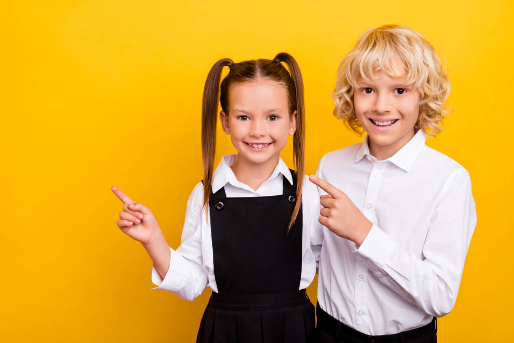Fotografie promotér školáci indikují ukazováček prázdný prostor oblečení školní uniforma izolované žluté pozadí - Fotografie, Obrázek