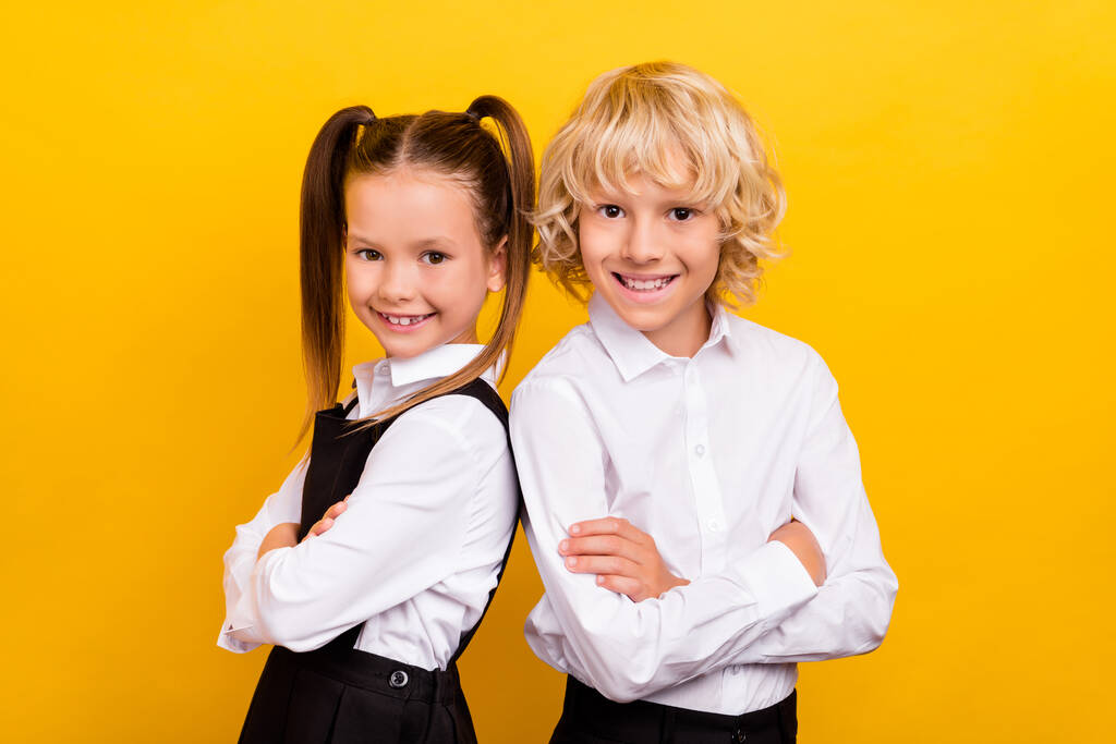 Foto von zwei selbstbewussten Schulkindern gekreuzte Hände tragen Schuluniform isoliert gelben Hintergrund - Foto, Bild