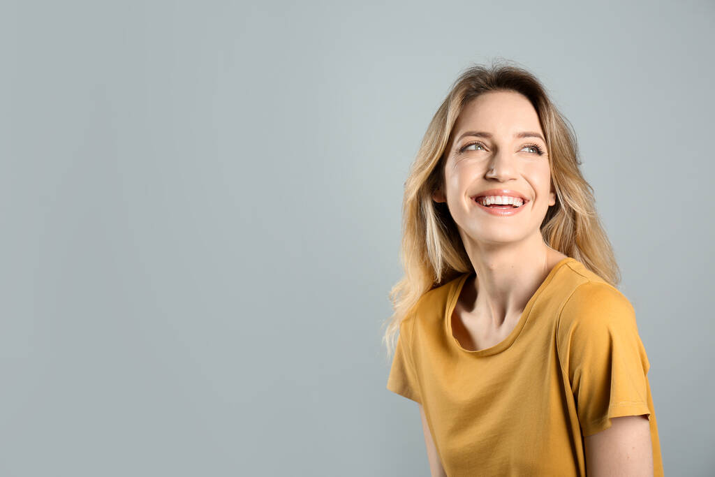 Retrato de mujer joven feliz con hermoso cabello rubio y sonrisa encantadora sobre fondo gris. Espacio para texto - Foto, Imagen
