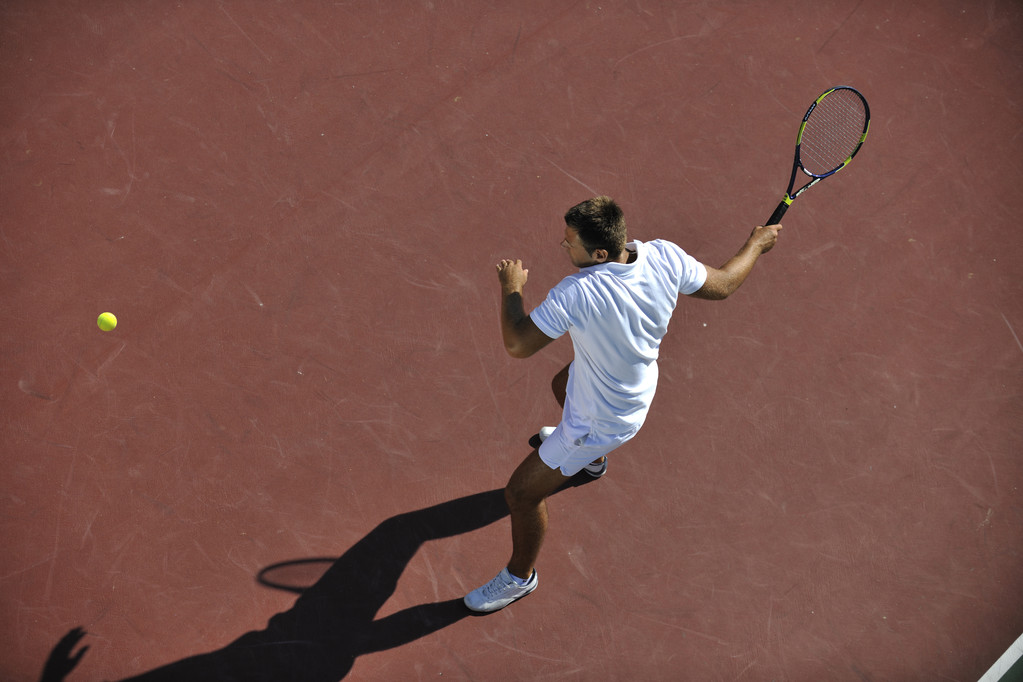 Nuori mies pelata tennistä ulkona oranssi tenniskenttä aikaisin aamulla
 - Valokuva, kuva