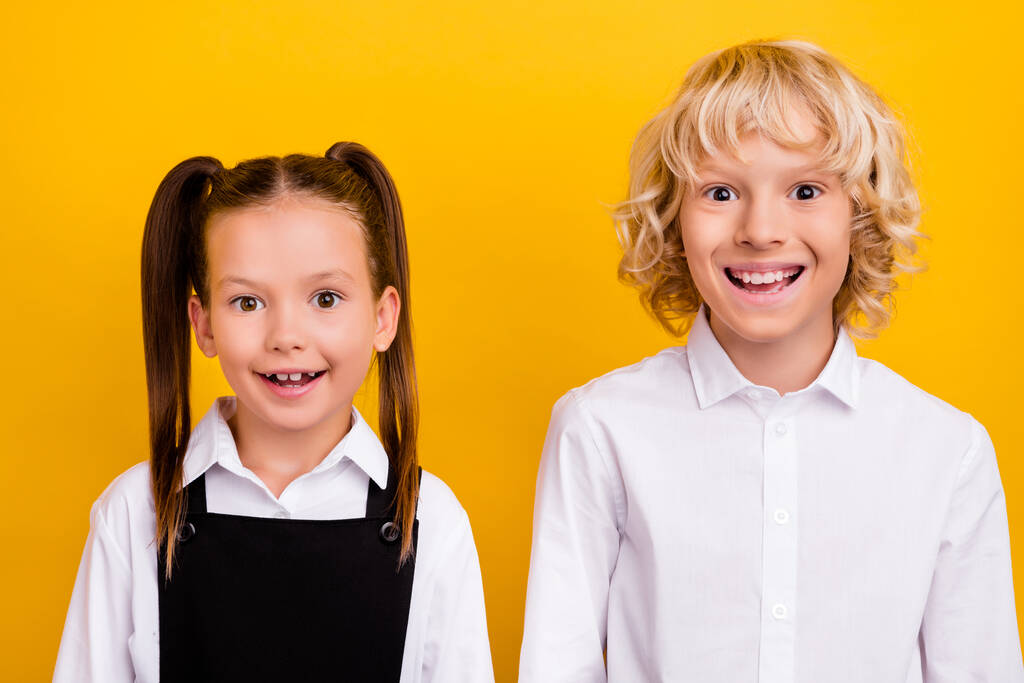 İki komik pozitif öğrencinin fotoğrafı parlak beyaz gülümseme okul üniforması giyiyorlar izole edilmiş sarı arka plan. - Fotoğraf, Görsel