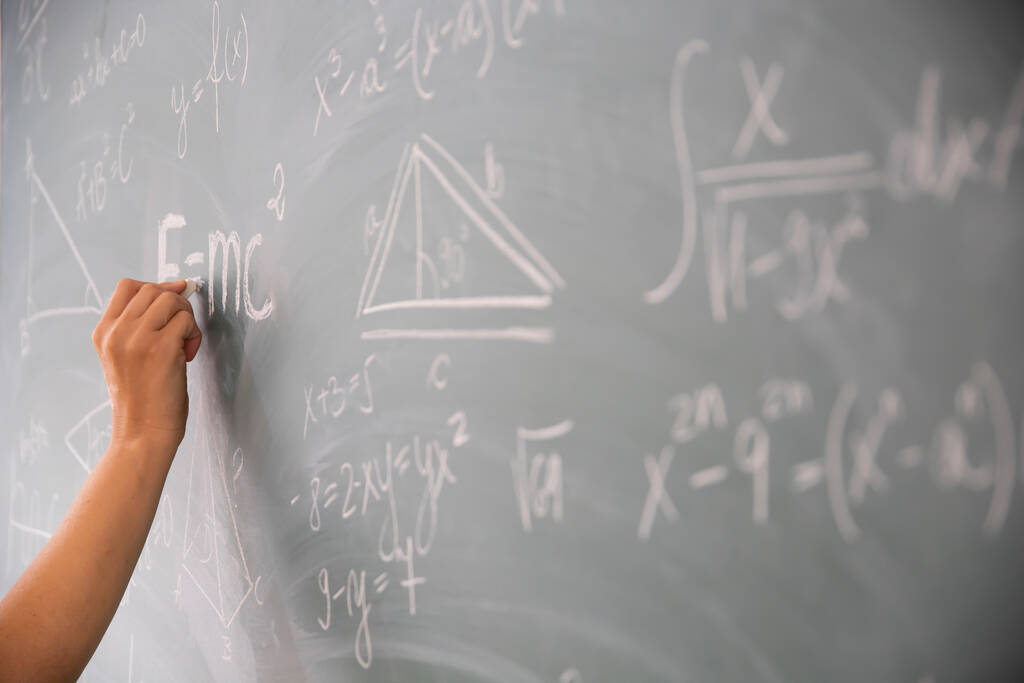 Közelkép egy krétát tartó kézről, és matematikai egyenleteket ír a táblára. Oktatási koncepció. - Fotó, kép