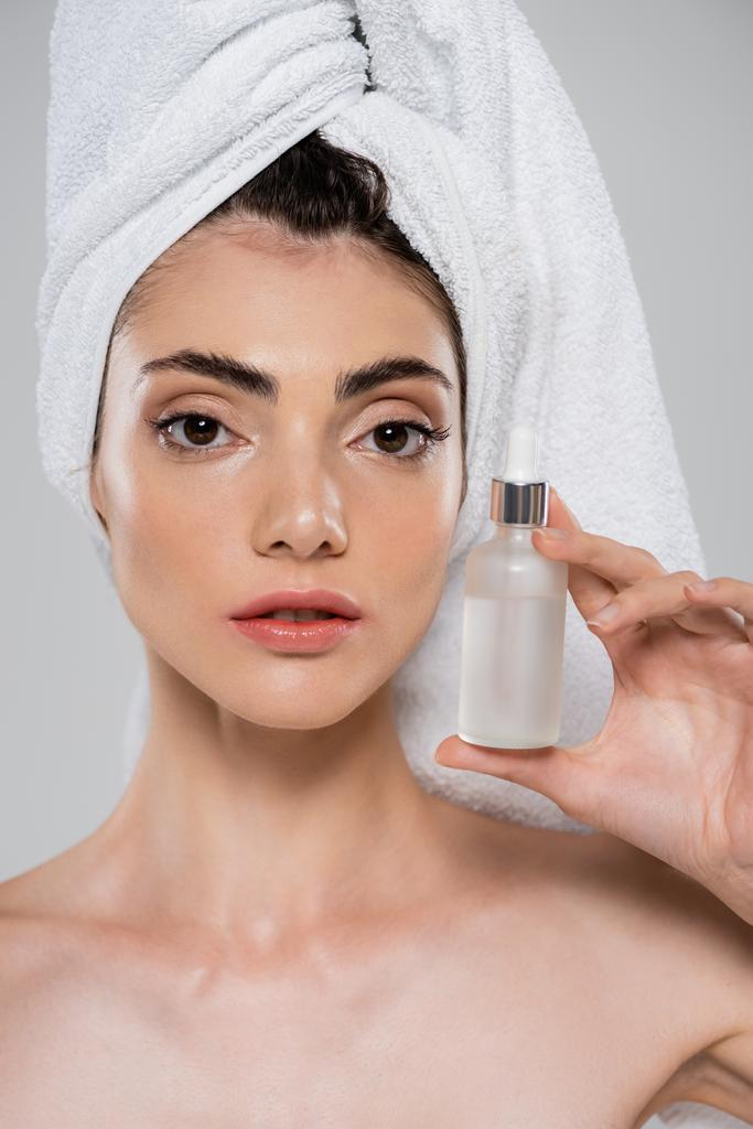 young woman with towel on head holding bottle with serum isolated on grey - Photo, Image