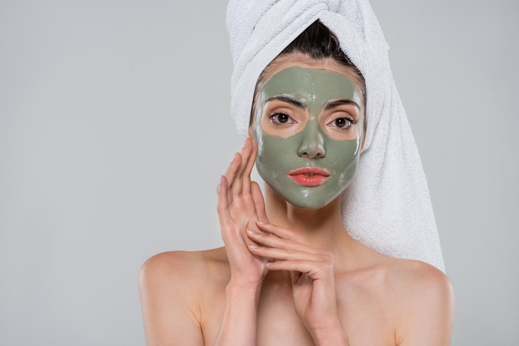 młoda kobieta z ręcznikiem na głowie i zieloną maską glinianą patrząc na kamerę odizolowaną na szaro - Zdjęcie, obraz