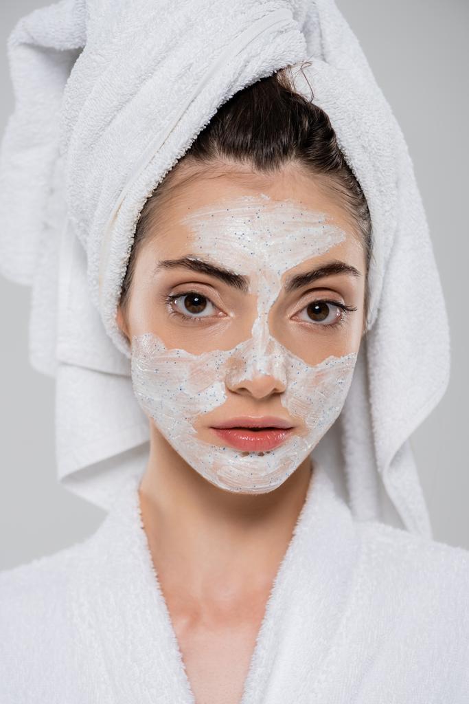молодая женщина с полотенцем на голове и лицо скраб изолирован на сером  - Фото, изображение