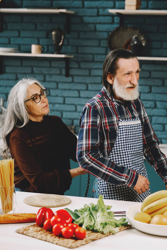 Oudere paar zet op schorten voor het bereiden van voedsel in de keuken - Foto, afbeelding