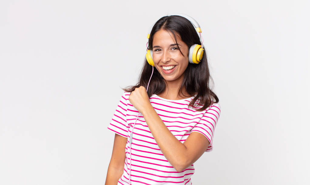νεαρή ισπανίδα γυναίκα αισθάνεται ευτυχισμένη και αντιμετωπίζει μια πρόκληση ή γιορτάζει ακούγοντας μουσική με ακουστικά - Φωτογραφία, εικόνα