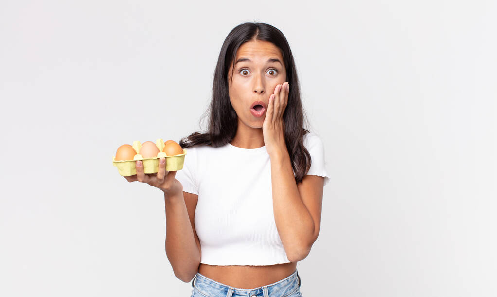 молодая латиноамериканка, шокированная и напуганная, держит коробку с яйцами - Фото, изображение