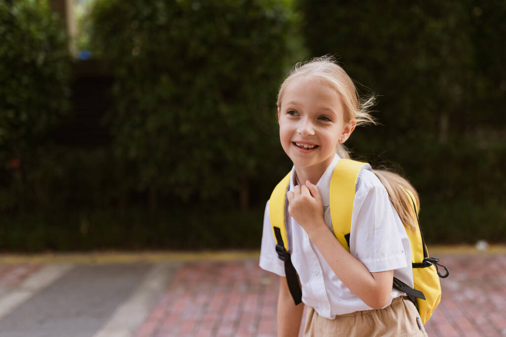 Koulutyttö palaa kouluun kesälomien jälkeen. Lapsi univormussa hymyilee aikaisin aamulla ulkona.  - Valokuva, kuva