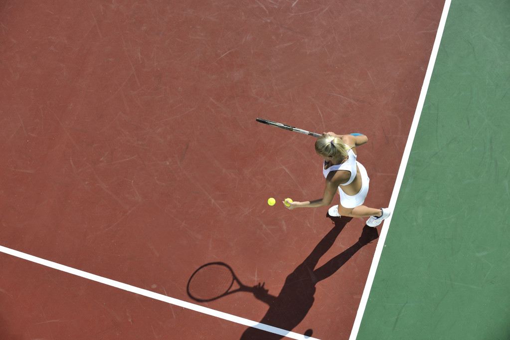 молода підтягнута жінка грає в теніс на відкритому повітрі на помаранчевому тенісному полі рано вранці
 - Фото, зображення